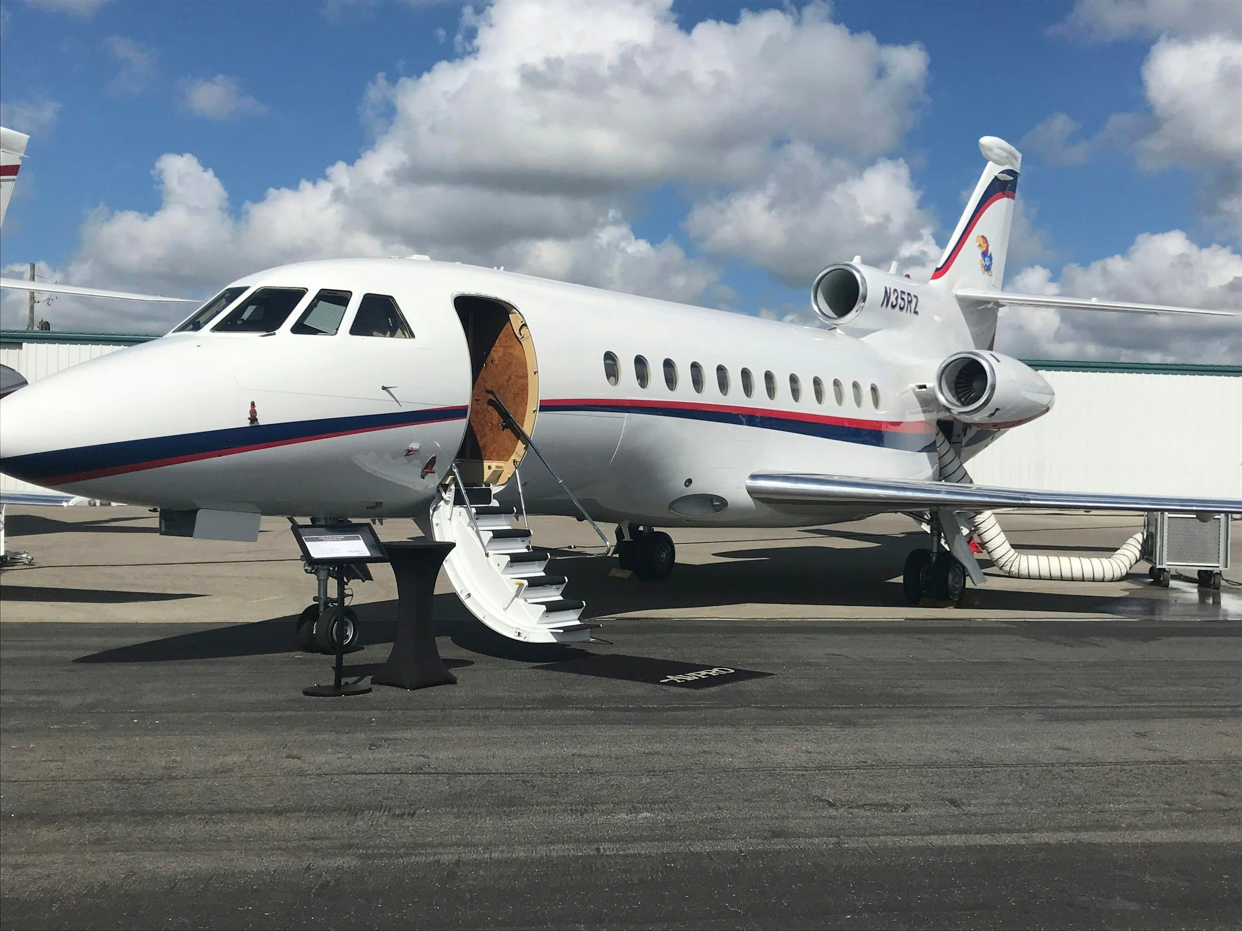 Private jet airplane parked on tarmac with stairs leading to open door, cloudy sky background.