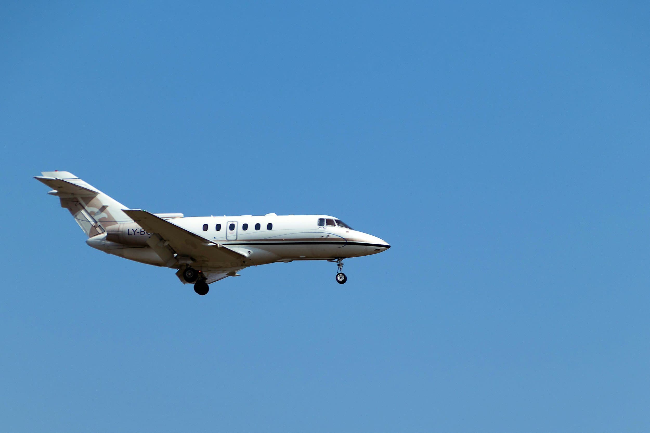 A white private jet flying in a clear blue sky.