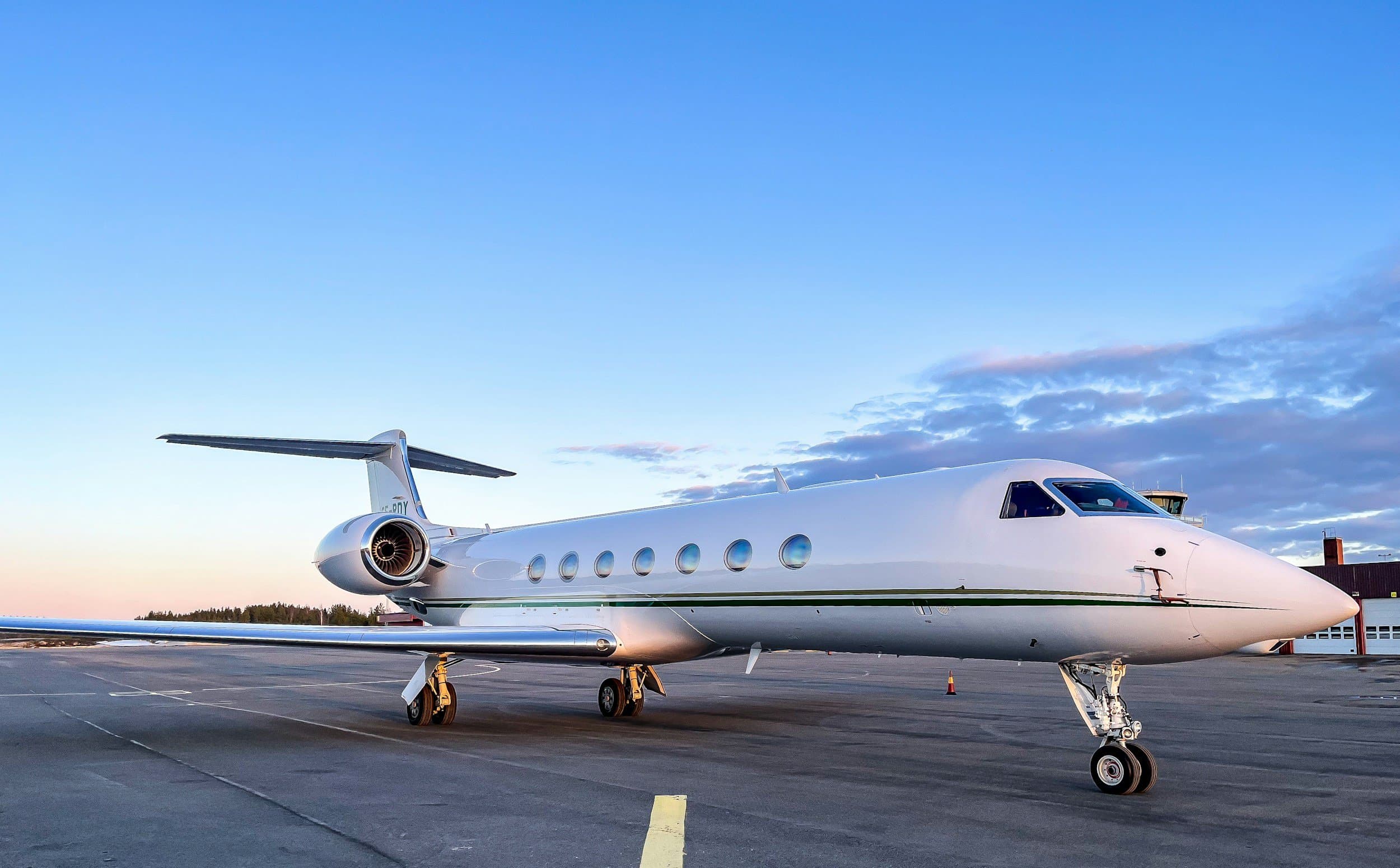White private jet parked on an airport tarmac during sunset with a partly cloudy sky in the background.